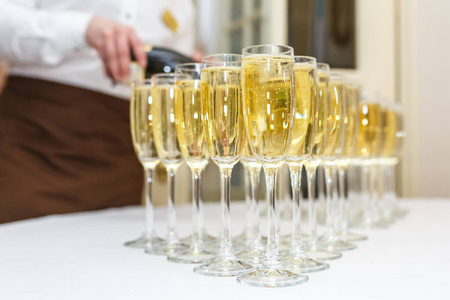 在灯光背景下的接待宴会桌上放了很多带香槟的模糊眼镜