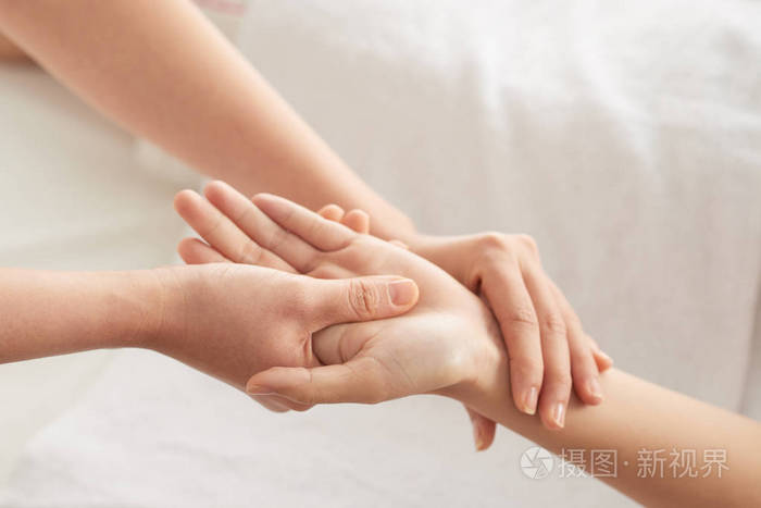 匿名治疗师在水疗沙龙按摩期间揉搓女性客户的手腕和手掌