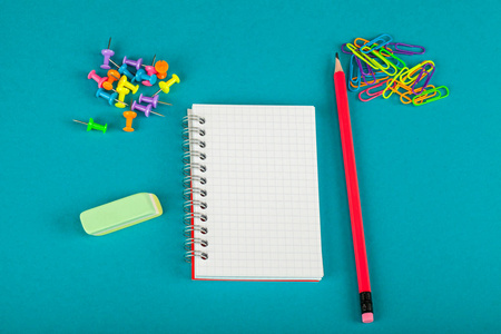 白色笔记本铅笔和彩色回形针在蓝色背景学校用品概念