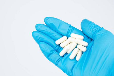 胶囊药物在手特写。 在照片右边交一只蓝色橡胶手套。 药片在医生的手掌上。 白色背景位置签名共空间