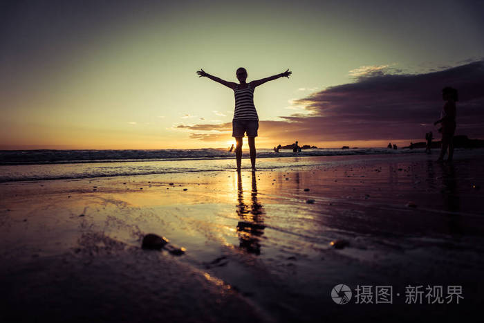 日落海滩女孩的剪影张开双臂在海上海岸自由概念