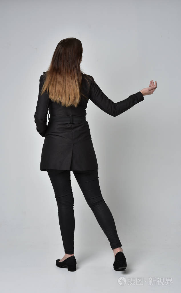 一个穿着黑色长外套的深色女孩的全长肖像站在灰色