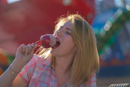 漂亮的年轻女人在公园里吃和咬红焦糖苹果照片