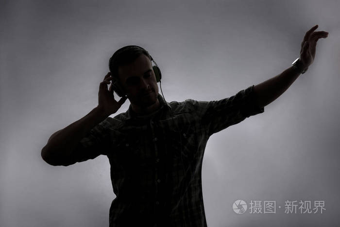 在灰色背景下听音乐的年轻人的剪影