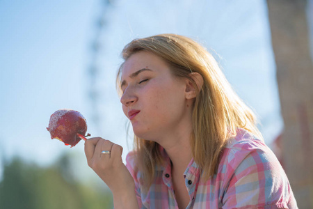 在阳光明媚的日子里，漂亮的年轻女人在公园里吃和咬红焦糖苹果