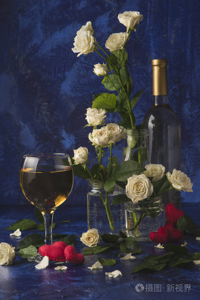 一杯酒,一束白色玫瑰和红色的心,蓝色背景上有烟雾. 情人的假期.