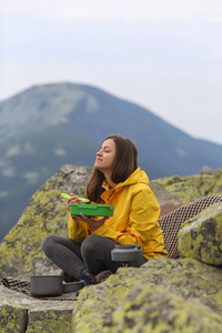 穿黄色夹克的年轻女人在山顶野餐。