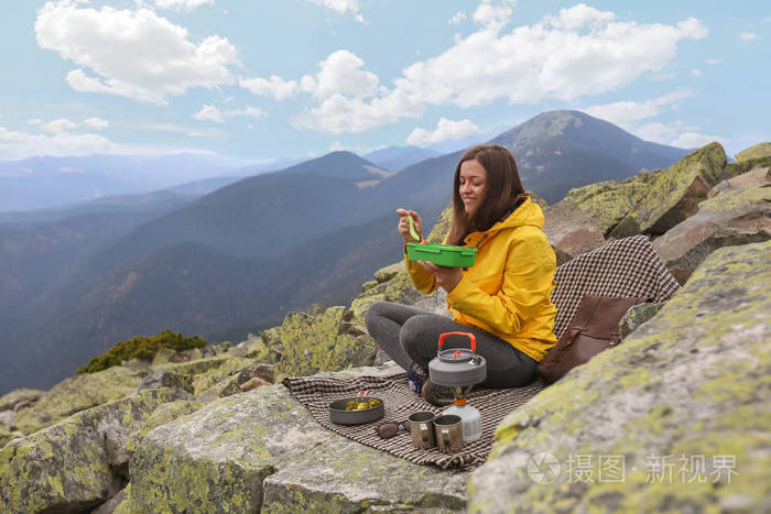 穿黄色夹克的年轻女人在山顶野餐
