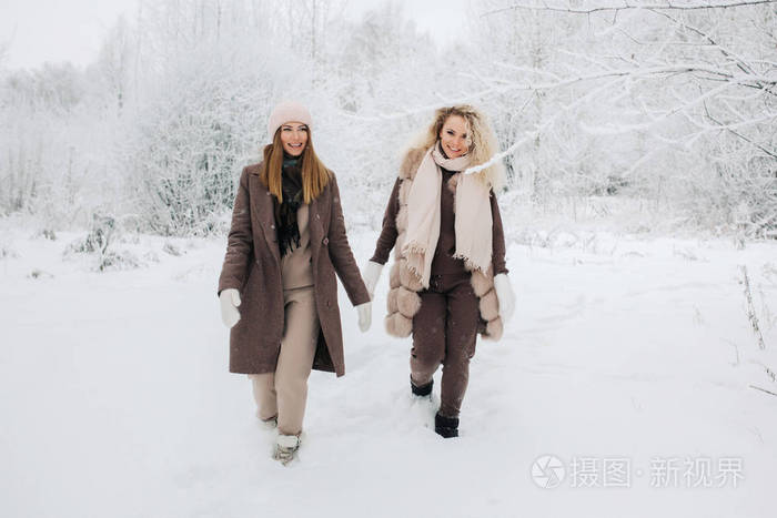 两个金发碧眼的女人在冬天的森林里戴帽子走路的肖像