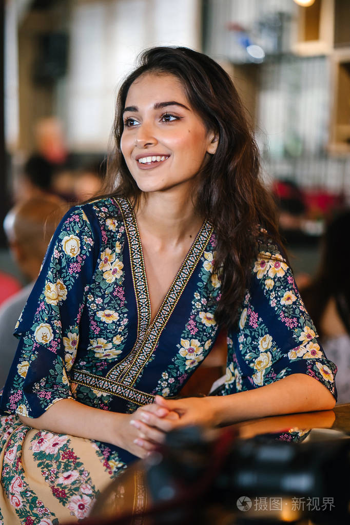 一个年轻,自信和有魅力的印度亚洲女孩在一家灯火通明的时髦咖啡馆的