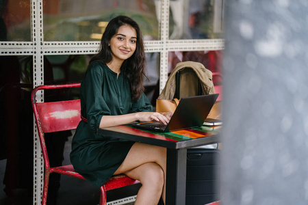 年轻的大学生印度亚裔女性白天在一张桌子上学习和工作笔记本电脑
