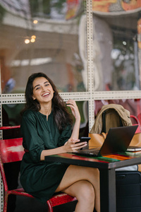 年轻的印第安女人，白天在咖啡馆里休息，不用在笔记本电脑上学习或工作，她正在检查她的智能手机