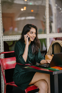 年轻的印第安女人，白天在咖啡馆里休息，不用在笔记本电脑上学习或工作，她正在检查她的智能手机