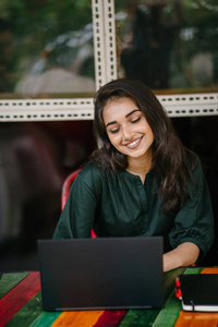 年轻的大学生印度亚裔女性白天在餐桌上学习和工作她的笔记本电脑