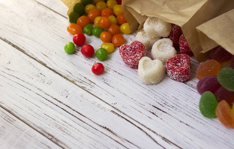 圆形彩色糖果和果酱放在木桌上的纸袋里，明亮的糖果，白色的背景
