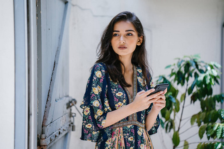 一位年轻迷人美丽的印度亚洲女性的肖像，她穿着连衣裙和太阳镜，带着智能手机