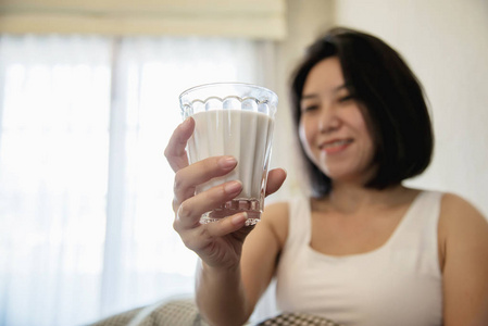 亚洲女人早上醒来后喝牛奶，坐在床上享受保健的概念