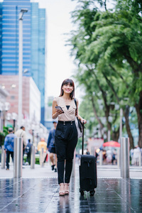 吸引人的亚洲中国女人在她的智能手机上通过她的搭便车应用程序。 4.她随身带着行李，穿着时髦的工作服