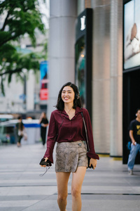 美丽的韩国女人穿着优雅的衬衫和短裤跳舞，她走在城市的一条街上，戴着耳机