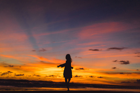 日落时海滩上的人。那个女孩在夕阳的背景下跳跃。