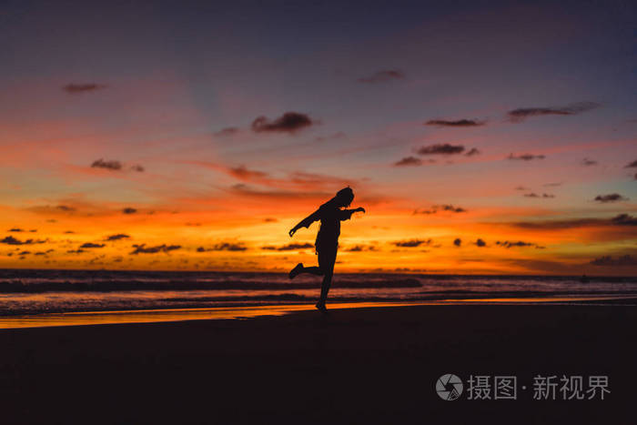 日落时海滩上的人那个女孩在夕阳的背景下跳跃