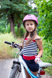 夏天骑自行车时戴着粉红色头盔的小可爱女孩