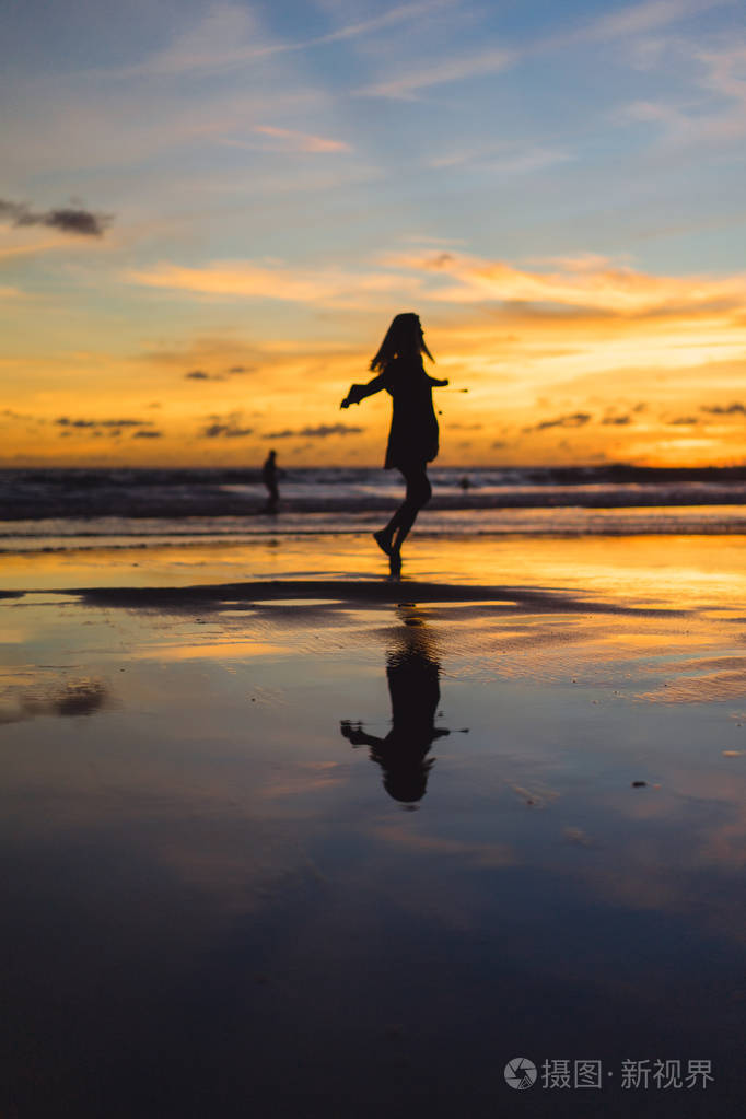 日落时海滩上的人. 那个女孩在夕阳的背景下跳跃.
