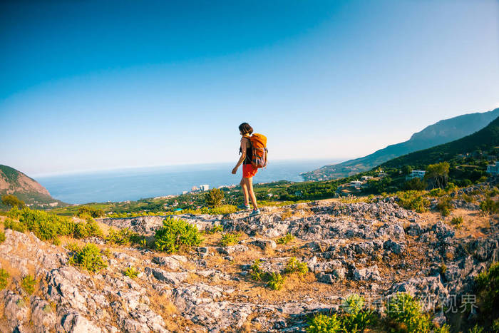 一个背着背包的女人站在岩石上. 爬到顶端. 去风景如画的地方旅行.