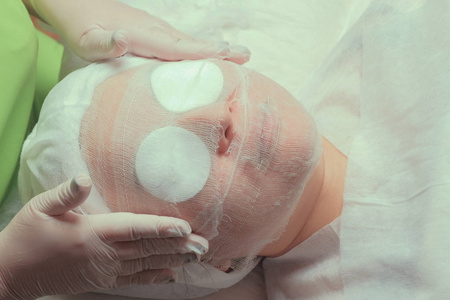 一个美容师或医生在一个亚洲女人的脸上贴上纱布绷带.用棉垫闭上眼睛.