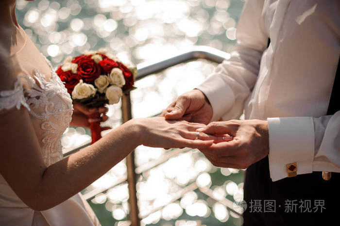 在大海的背景下, 给温柔的新娘手指戴上金色的结婚戒指