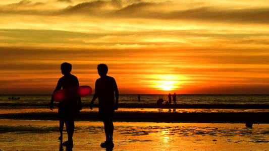 日落在美丽的海滩景色中，许多人在黄昏前来到海里玩耍。日落在海滩上的剪影。