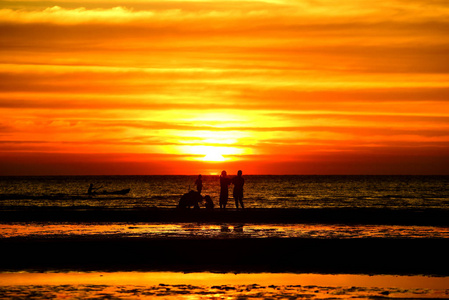 日落在美丽的海滩景色中，许多人在黄昏前来到海里玩耍。日落在海滩上的剪影。