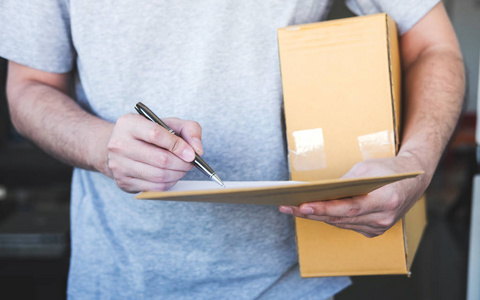 送货员将包裹箱交给收件人，并签署表格，年轻业主签署从邮寄快递上门送货服务收到的送货包裹，并与服务心合作。