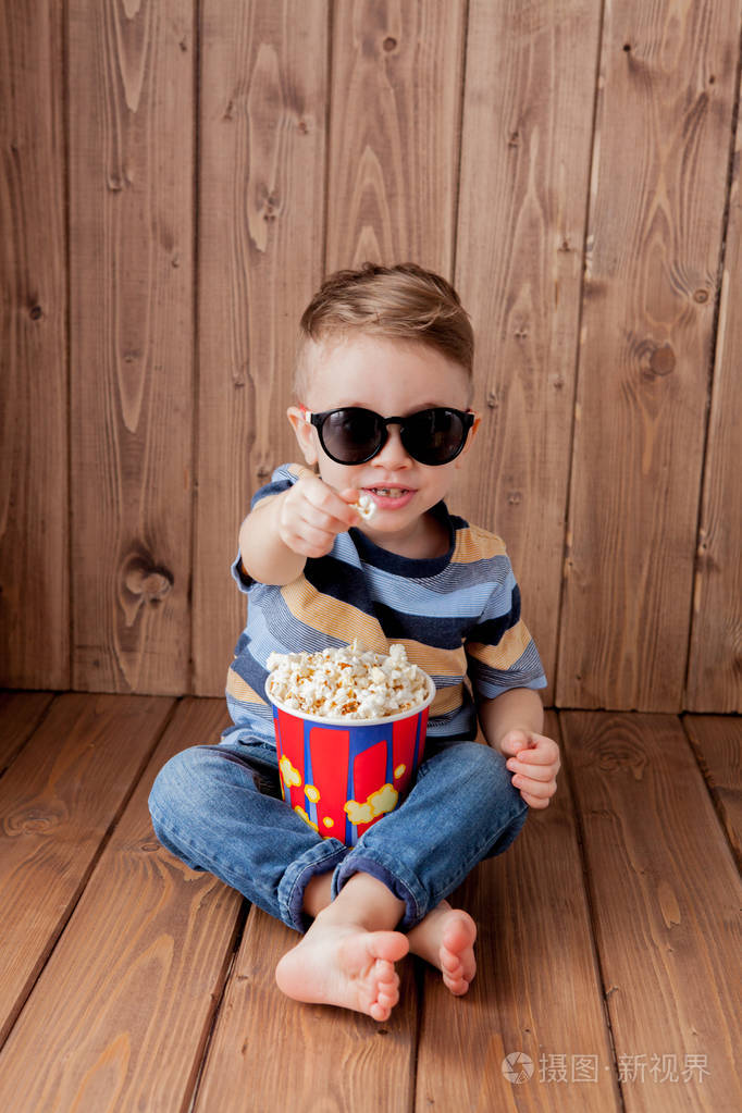 眼镜拿着桶爆米花在木制背景下吃快餐儿童童年生活方式的概念复制空间