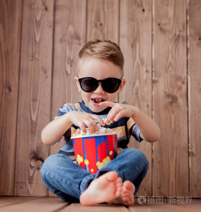 小可爱的孩子男孩2,3岁的3dima x影院眼镜,拿着桶爆米花,在木制背景下