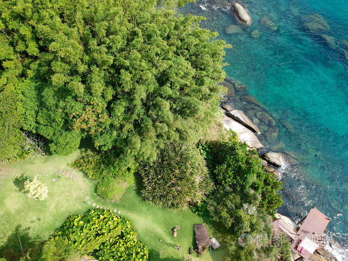 鸟瞰豪华住宅花园在热带森林周围的树木和旁边的海洋和蓝色绿松石水.