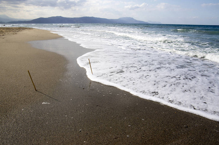 海水海浪沙石白海泡沫两根竹竿粘在沙滩上蓝天多云的天空