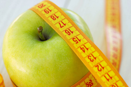 节食的概念。 带测量带的绿色苹果。 绿色的苹果测量米运动的苹果