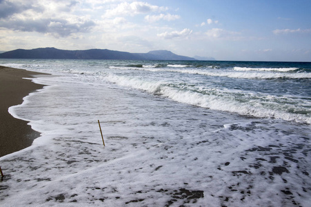 海水海浪沙石白海泡沫两根竹竿粘在沙滩上蓝天多云的天空