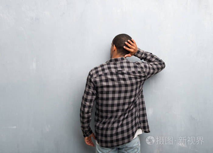 年轻的非裔美国男人背着格子衬衫回头看一边挠头