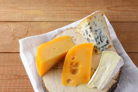 白色布上各种类型的奶酪。 卡蒙伯硬黄色奶酪在木板上。 白色餐巾纸上的乳制品。 复制空间