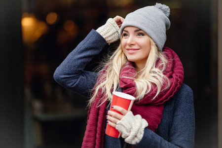 特写照片，年轻的金发女人喝咖啡，享受早晨在街上。 图像