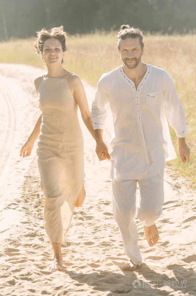 年轻的一对夫妇在夏天的沙滩上赤脚奔跑阳光明媚的一天手牵手