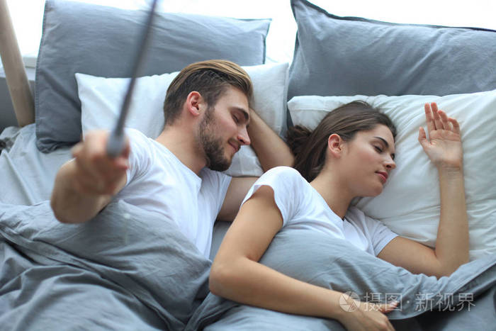 美丽的年轻情侣睡觉使自拍在床上的棍子