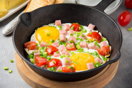 用火腿樱桃西红柿和春葱在黑锅里煎鸡蛋。 美味的早餐加土司和黄油。 经典英语