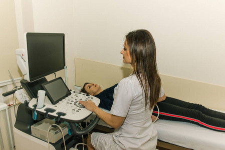 一种超声波医疗设备检查一个年轻的女孩，一个穿着浅色长袍的年轻医生