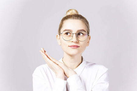 特写年轻美女的肖像，金发发髻，戴着时髦的圆形眼镜框和白色棉衬衫。 灰色隔离背景复制空间特写肖像