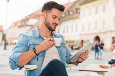 放松的男人喝着咖啡，低头看着平板电脑，坐在自助餐厅里的城市肖像画