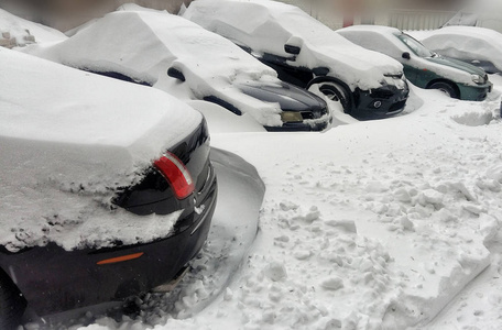 在十二月降雪期间，住宅区的停车场上覆盖着雪的汽车。