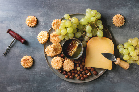 葡萄酒小吃。 奶酪，葡萄，坚果，奶酪，饼干，蜂窝与刀在黑暗的纹理背景。 平躺空间